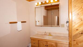 A bathroom with wooden cabinets, a sink, and a mirror with lights above it.