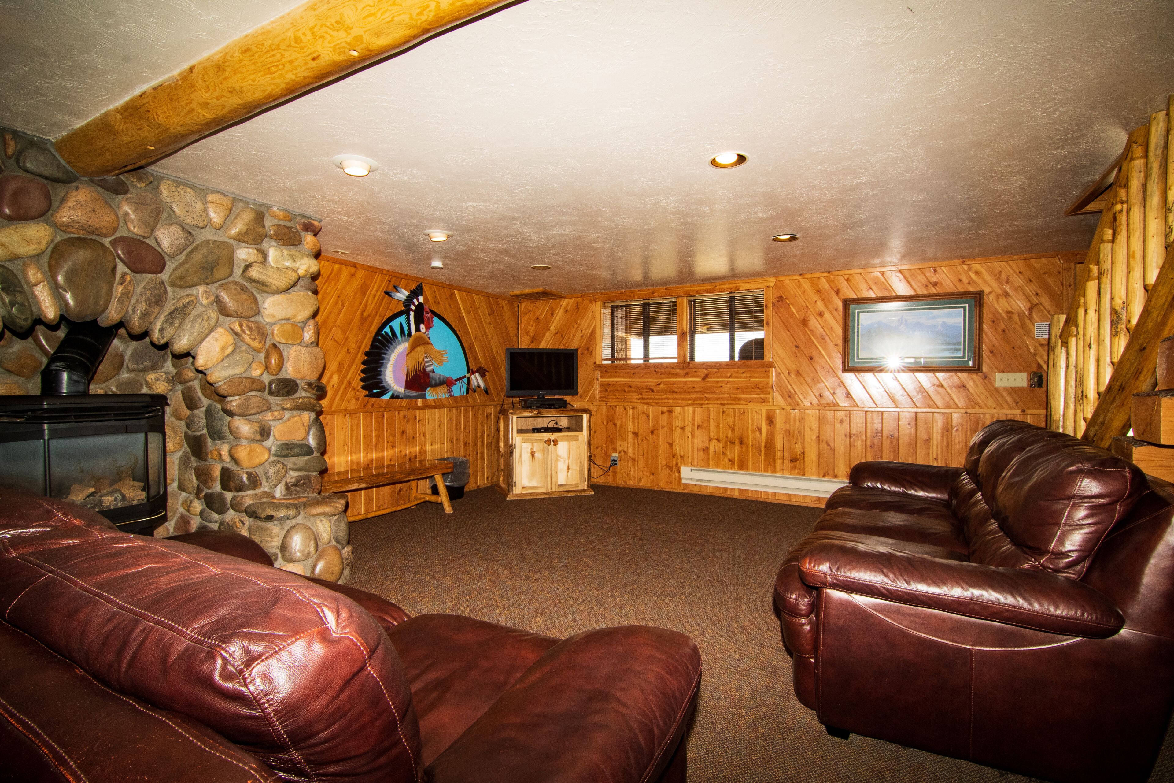 A cozy living room with a stone fireplace, wooden walls, and leather sofas.