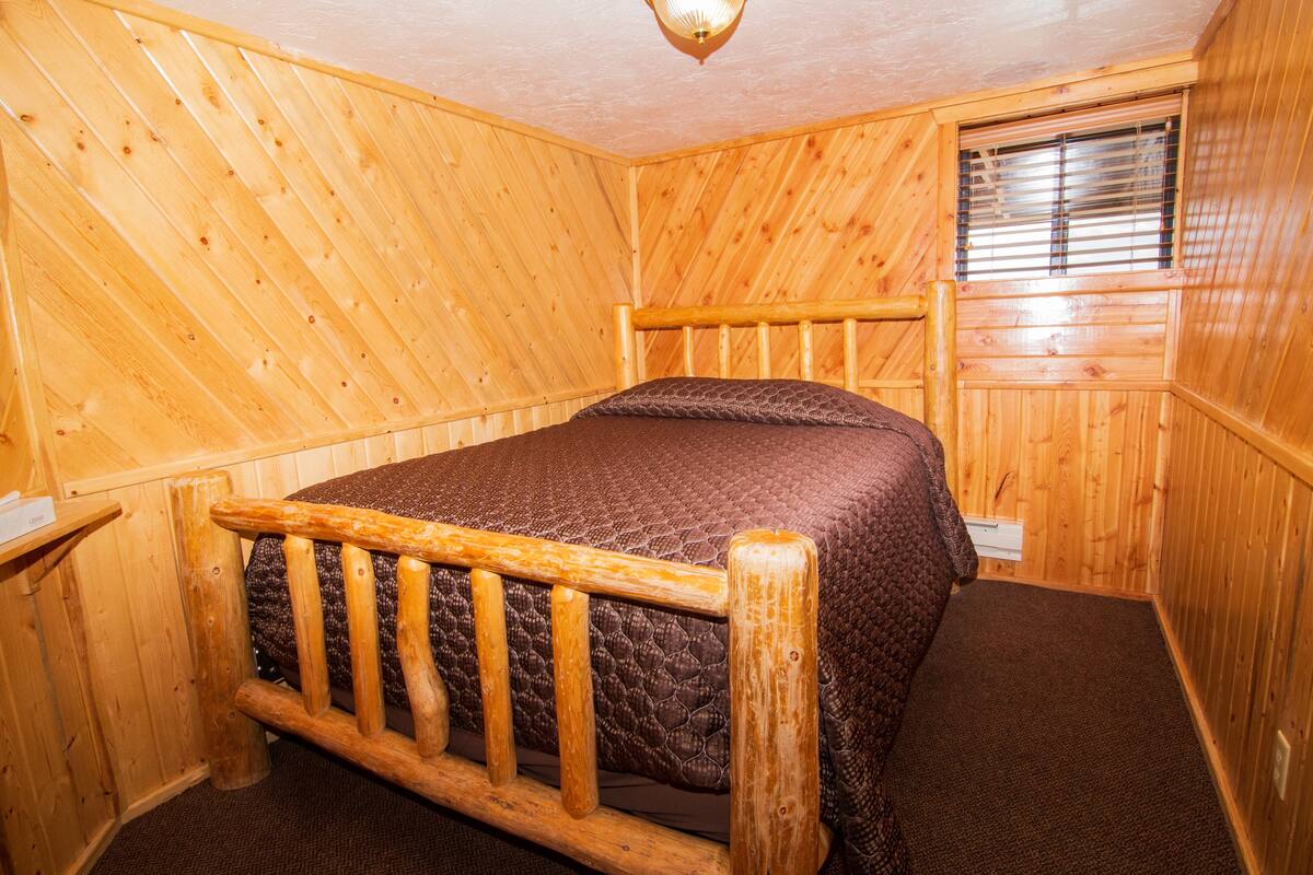 A wooden-paneled room with a bed, a window with blinds, and a wooden headboard.