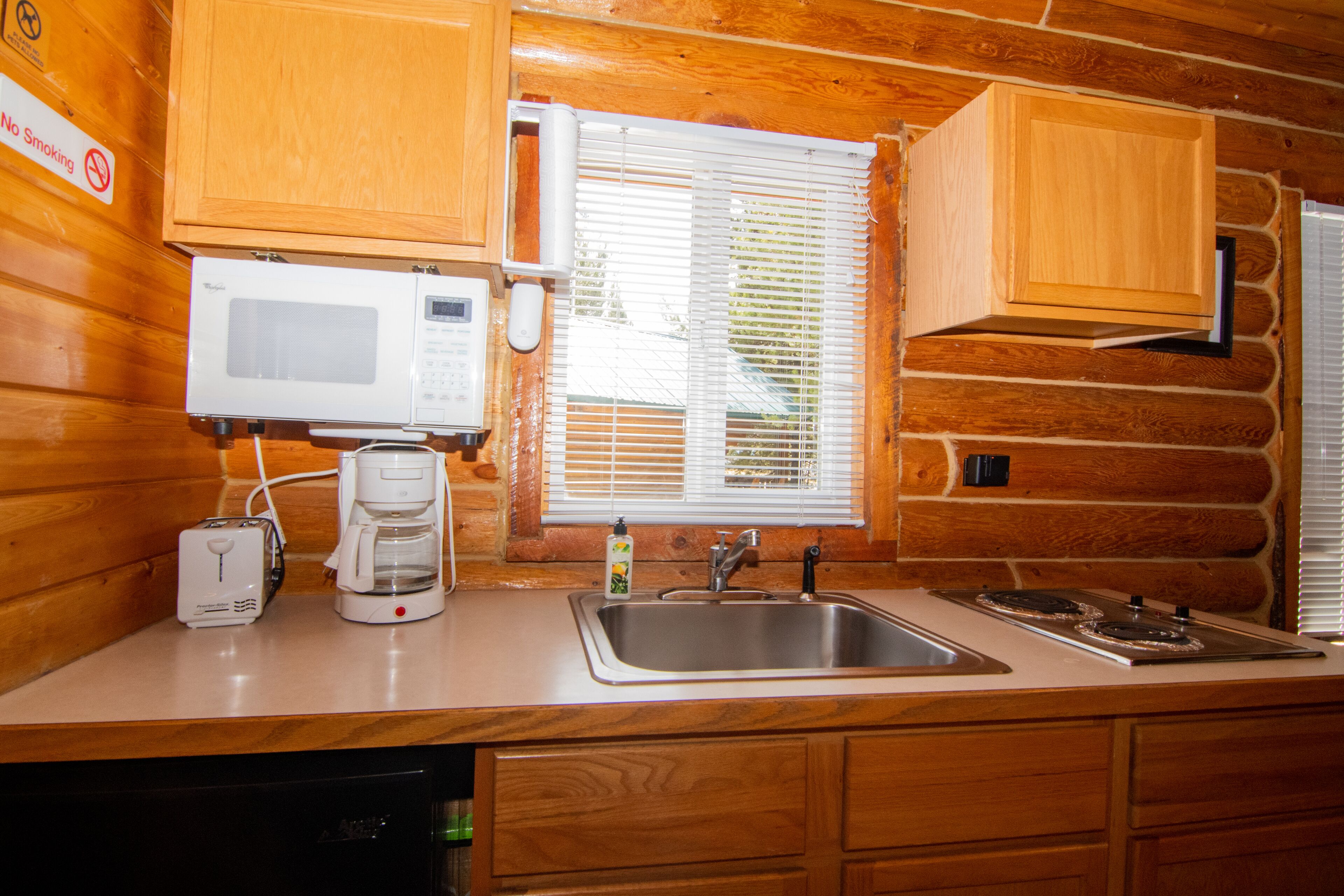 A kitchen with wooden cabinets, a microwave, a coffee maker, a sink, and a stove.