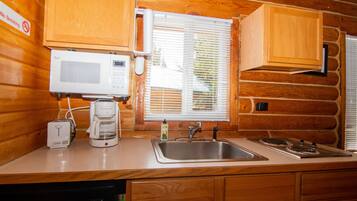 A kitchen with wooden cabinets, a microwave, a coffee maker, a sink, and a stove.