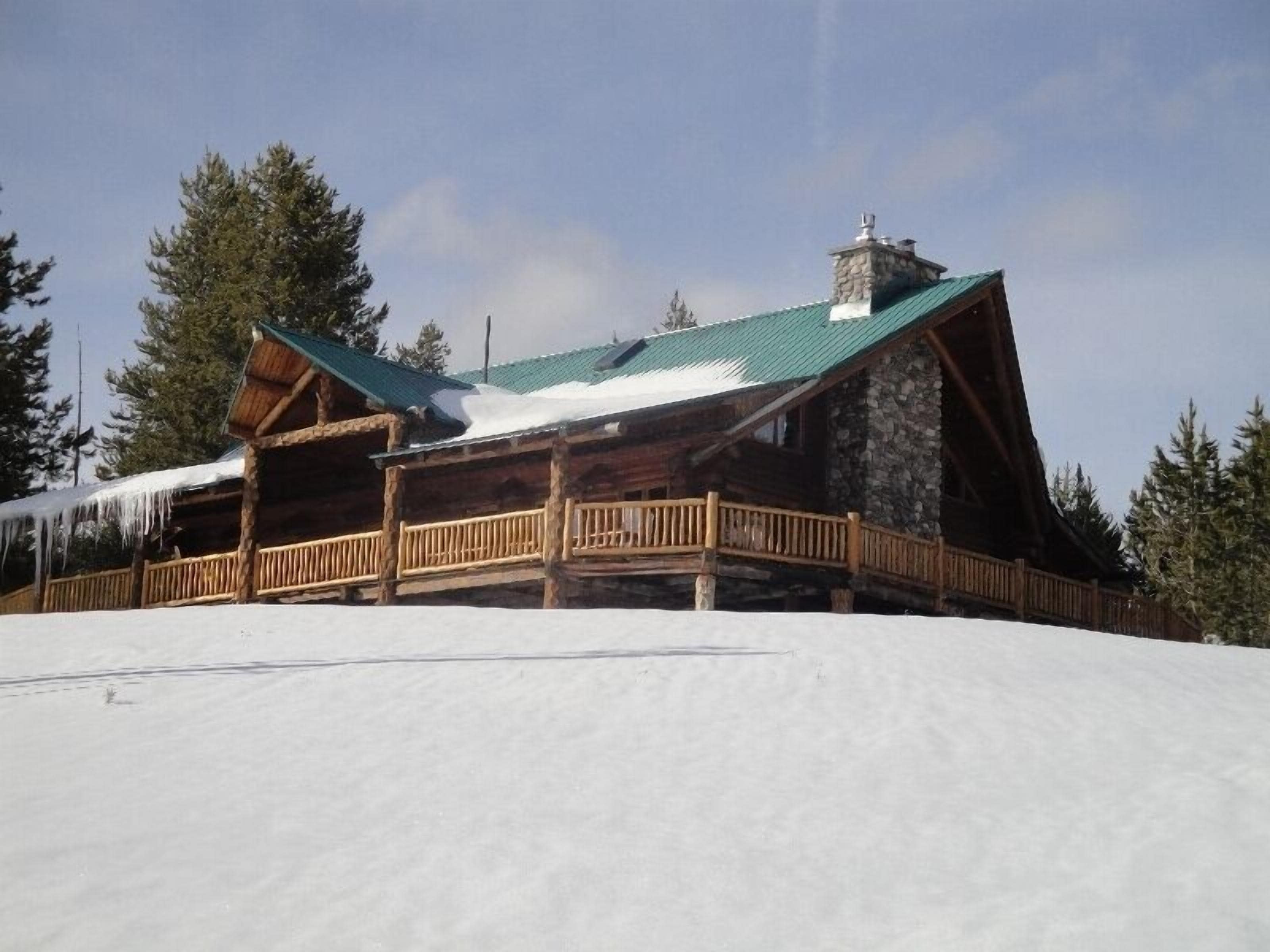 A log cabin with a stone chimney, wooden deck, and snow-covered surroundings.