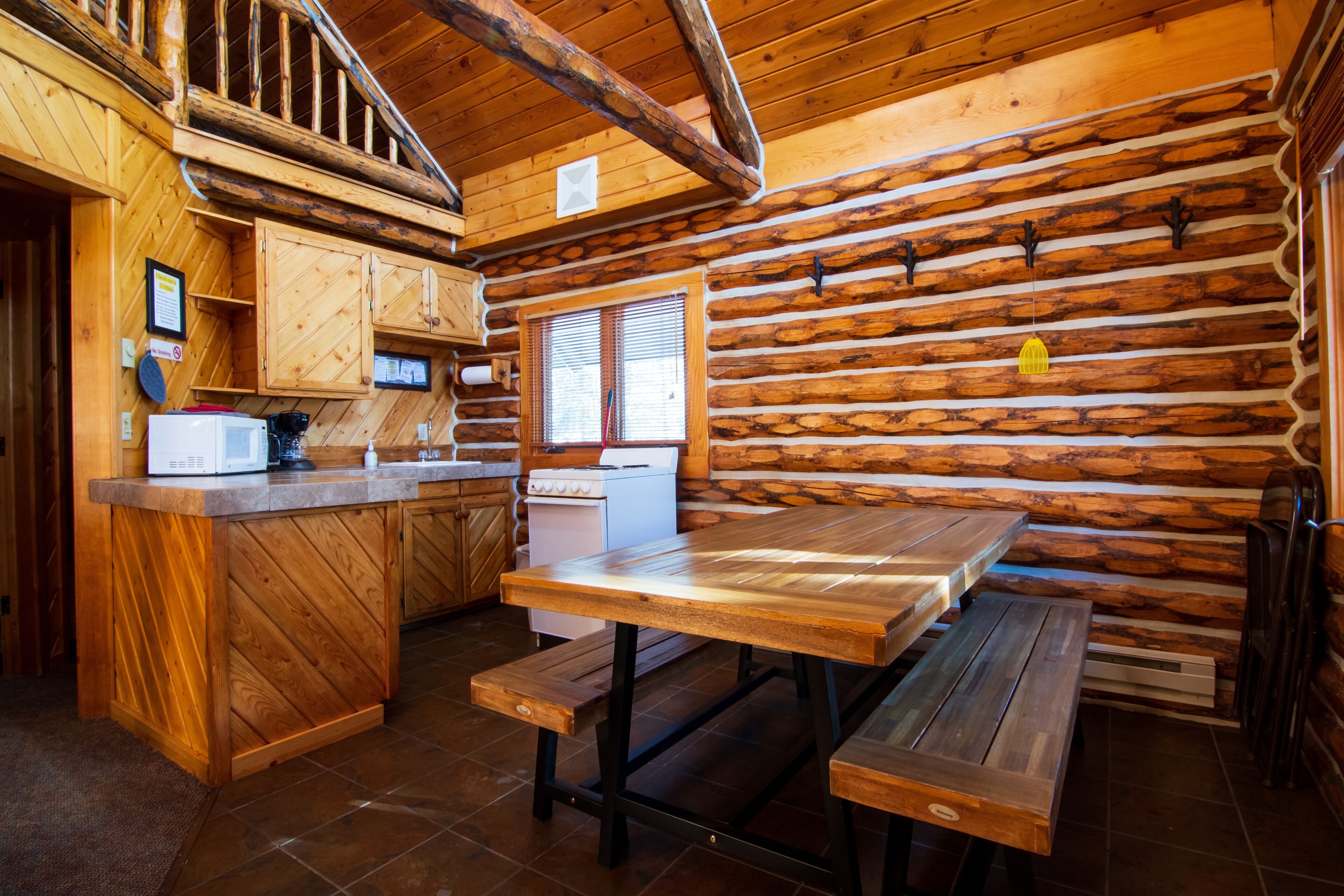 Een houten cabin met een keukenhoek, een houten eettafel en bankjes.
