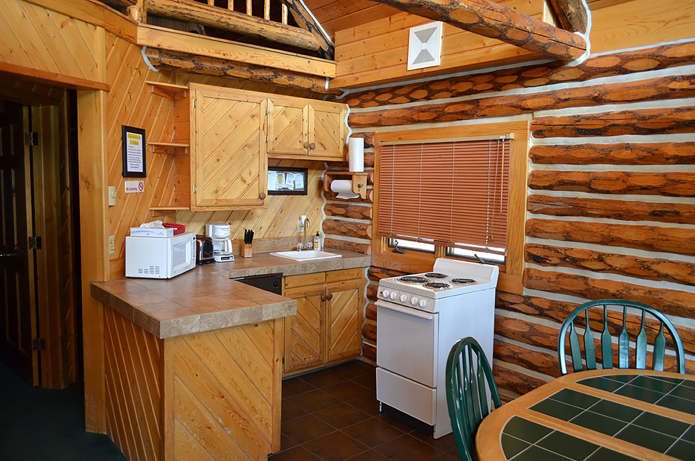 Una cocina de estilo rústico tipo cabaña, con paredes de madera, una estufa, un lavamanos y una mesa de comedor con sillas.