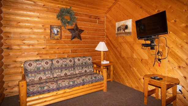Interior de uma cabana de madeira com um sofá de madeira, uma mesinha, um abajur, uma televisão e uma decoração em forma de estrela na parede.