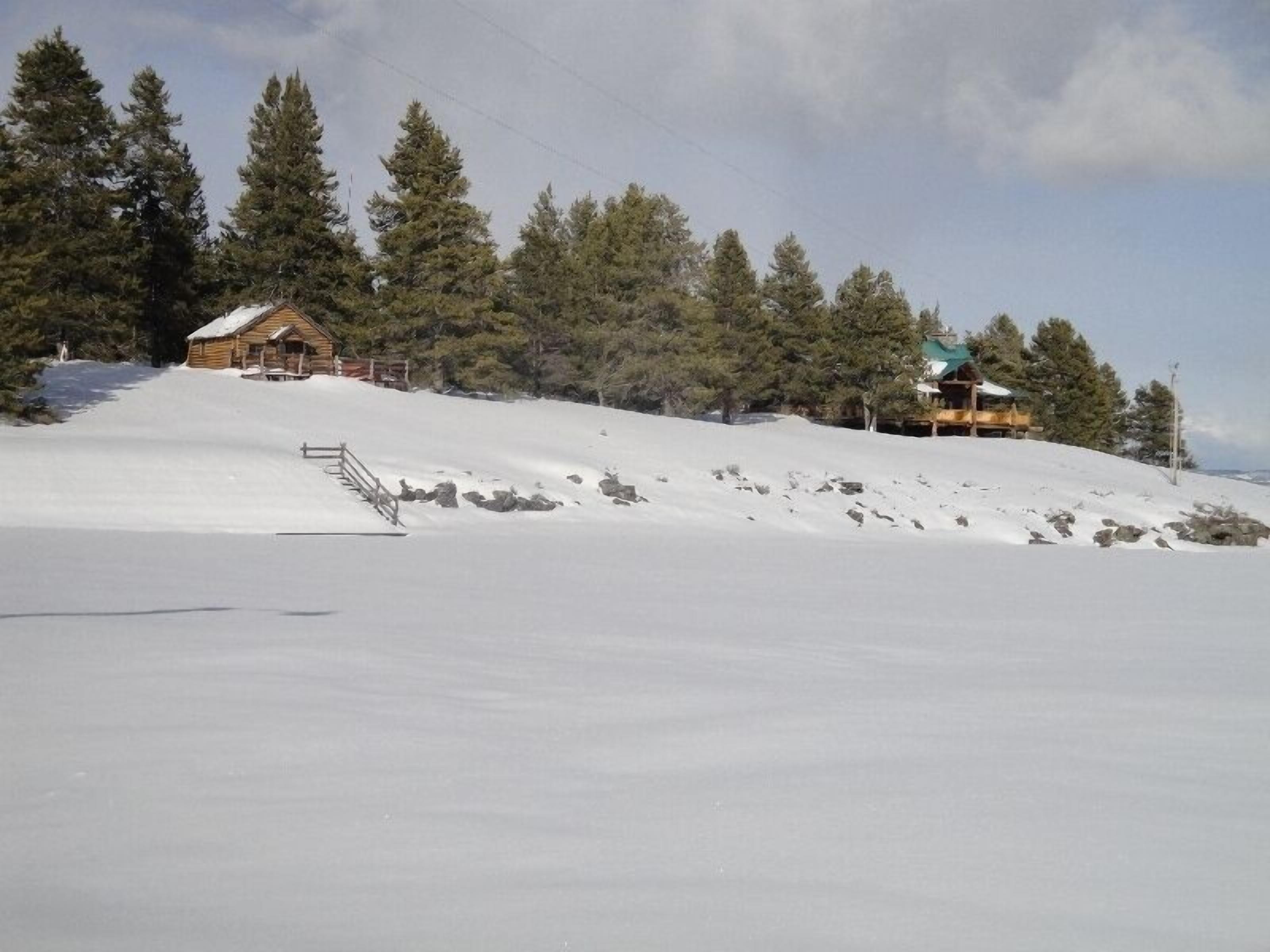 Une pente enneigée, avec un chalet en bois et un bâtiment plus grand doté d’un toit vert.