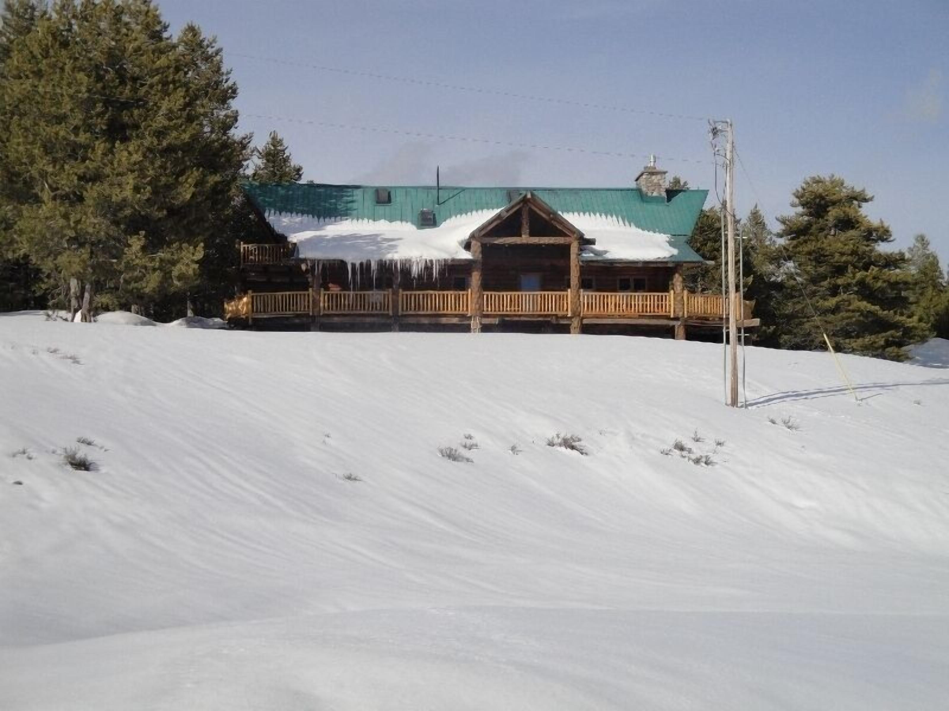 Una baita di legno con un tetto imbiancato dalla neve, circondata da alberi e da un paesaggio innevato.