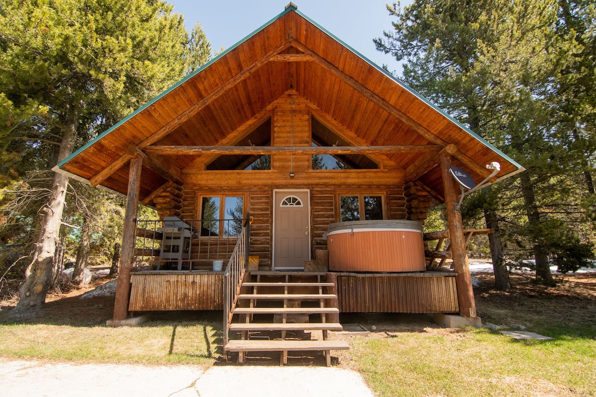 A wooden cabin with a pitched roof, a front door, and a hot tub.