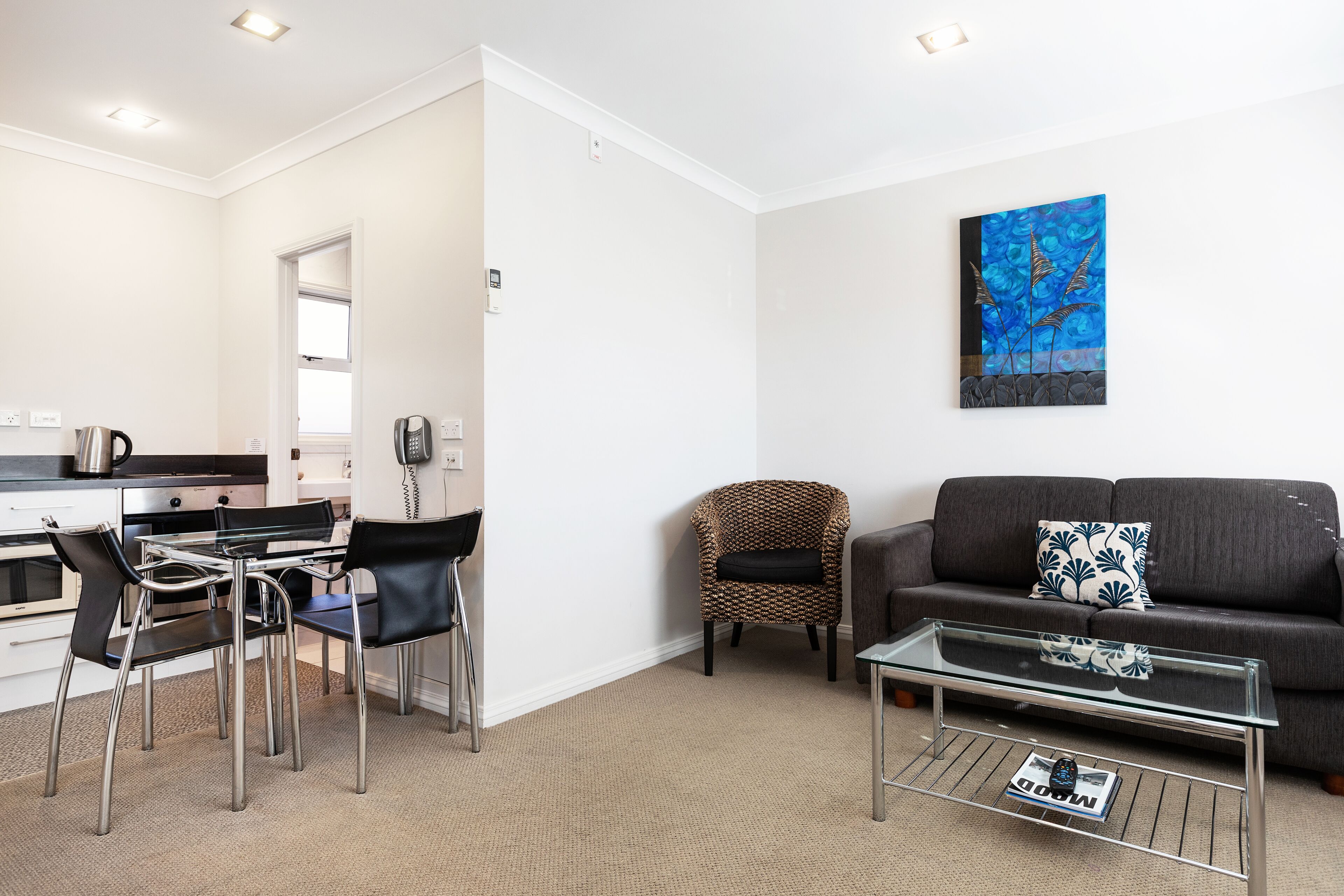 A modern living room with a glass coffee table, a sofa, and a dining area with chairs.