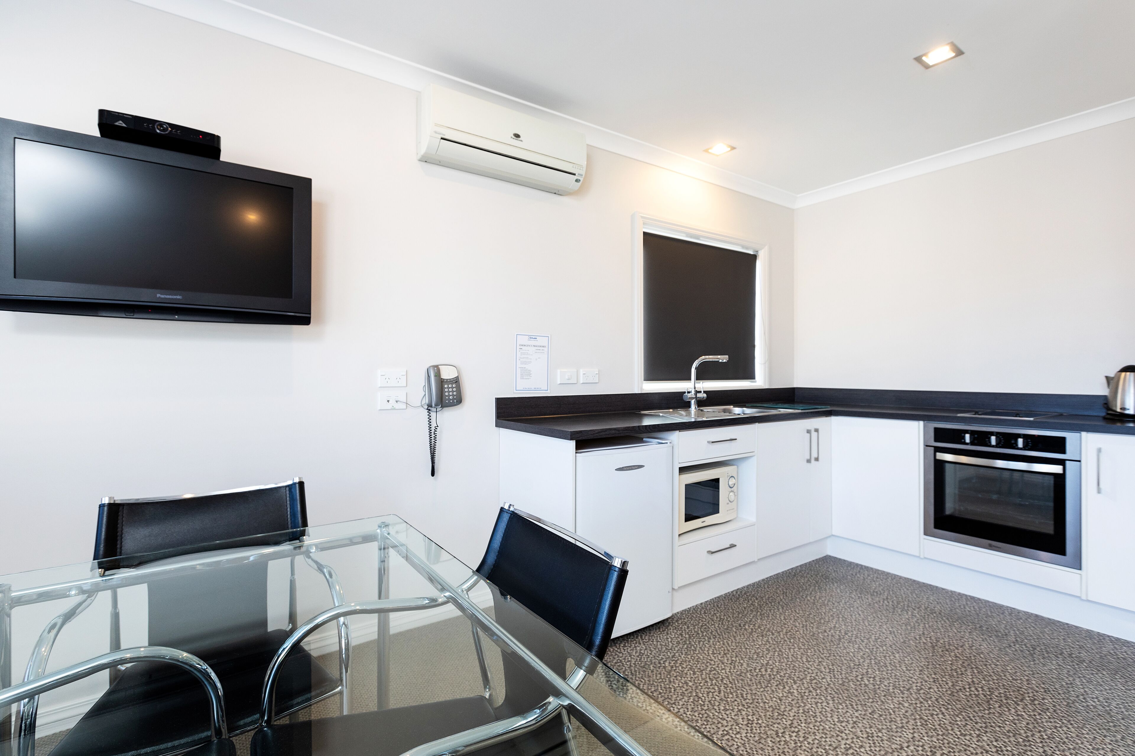 A modern kitchen with a flat-screen TV, built-in oven, and a glass dining table with chairs.