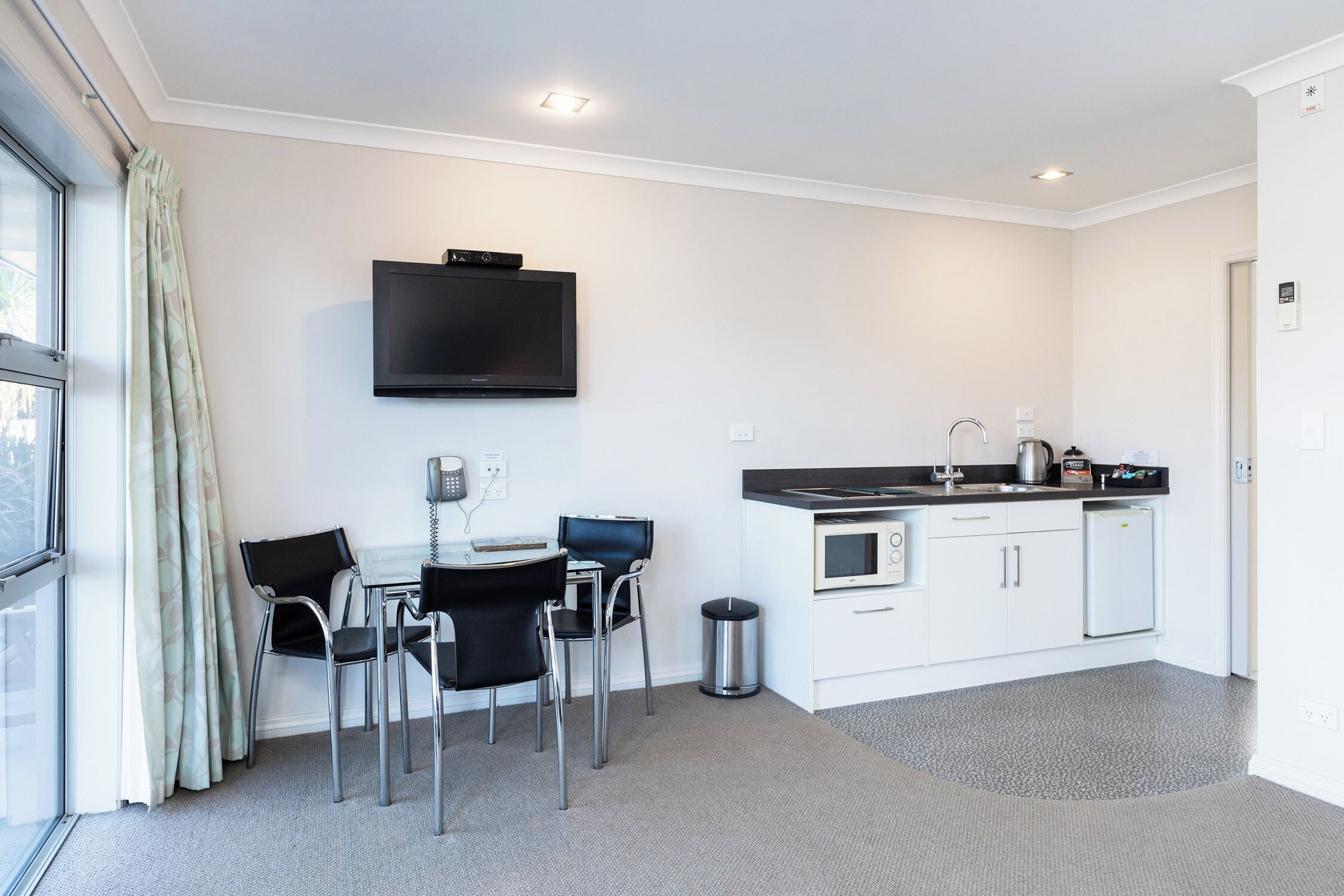 A modern kitchen with a flat-screen TV, a dining area with chairs, and a small refrigerator.