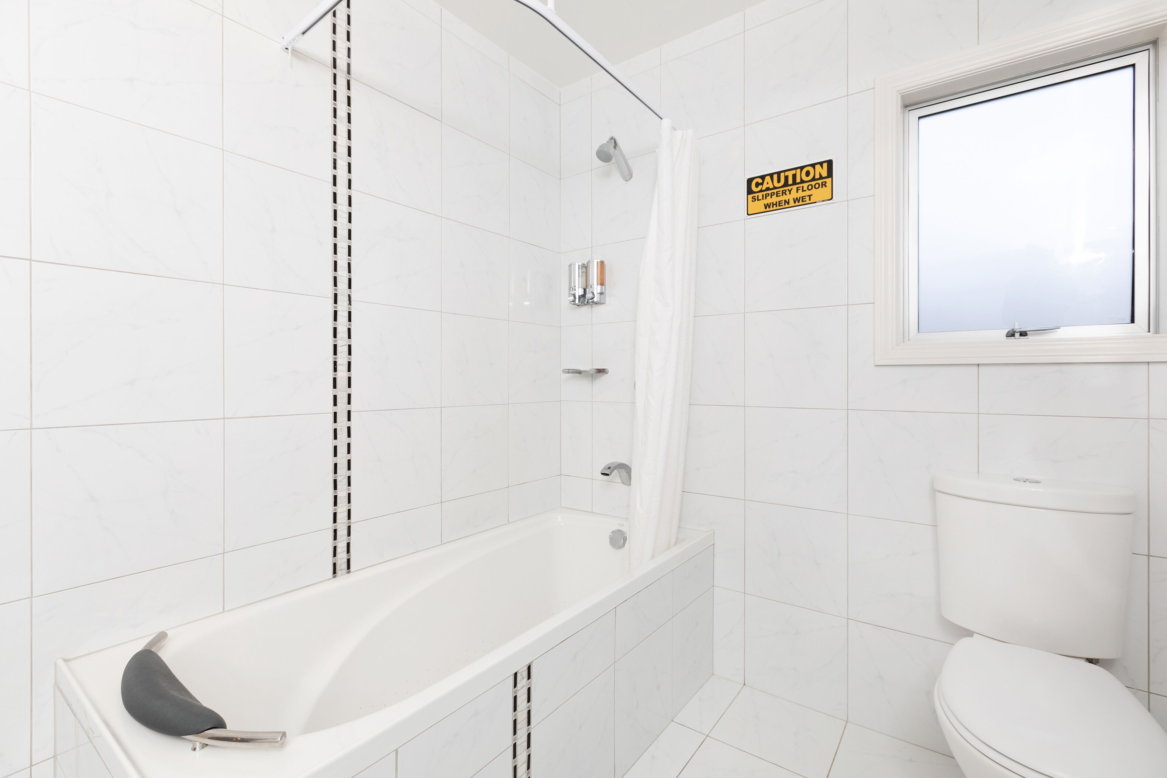A bathroom with a bathtub, toilet, and a caution sign on the wall.