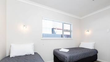 Una habitación con dos camas, una ventana con persianas e iluminación en la pared.