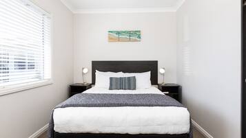 A neatly made bed with a white and gray comforter, a dark headboard, and a small bedside table with a lamp.