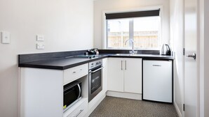 Une cuisine moderne avec des armoires blanches, un comptoir noir, un four encastré, un réfrigérateur et une fenêtre donnant sur une clôture en bois.