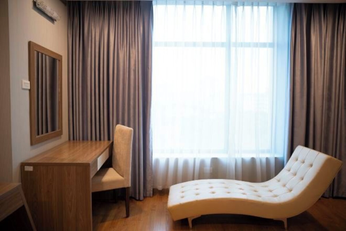 Una habitación moderna con un escritorio de madera, una silla acolchada y un sillón reclinable junto a un ventanal con cortinas.