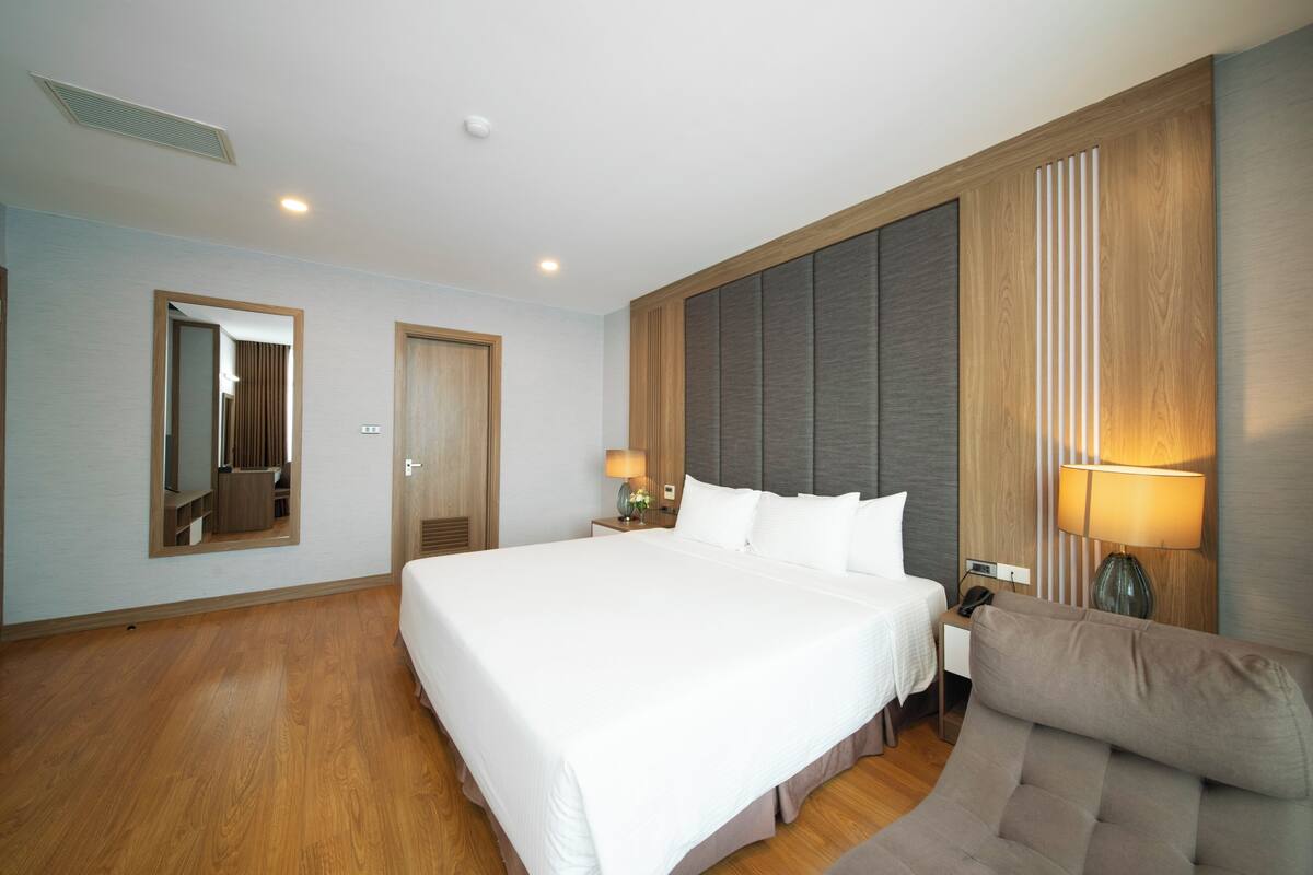 Una habitación de hotel moderna con una cama grande, un sofá, un espejo y una mesita de noche con una lámpara.