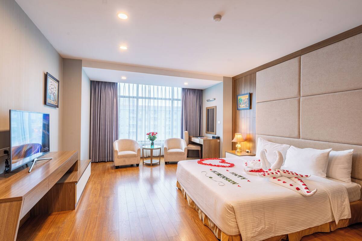 Habitación de hotel con una cama, un escritorio, un televisor y una ventana con cortinas.