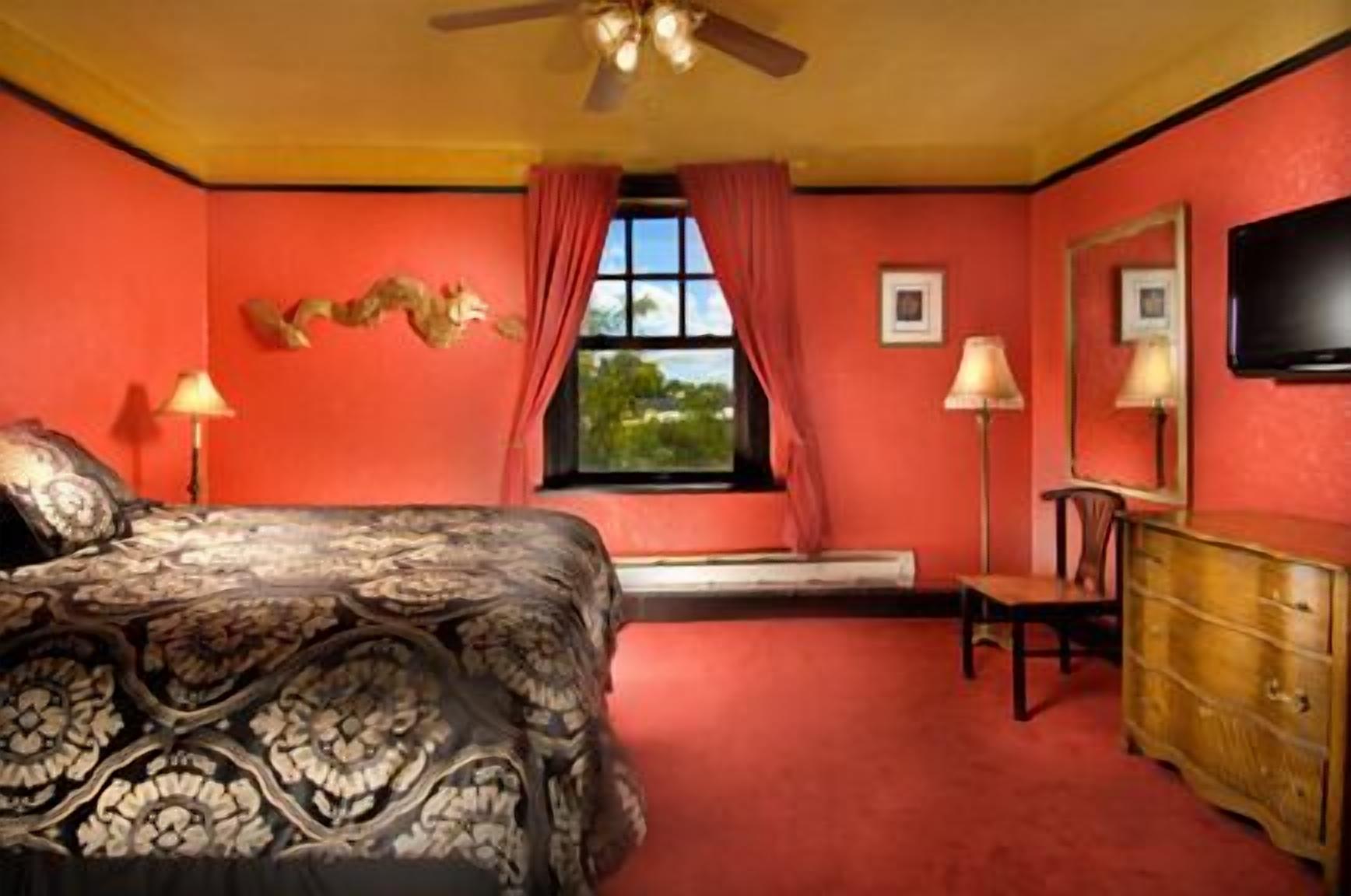 A bedroom with a bed, a dresser, a television, and a window with curtains.