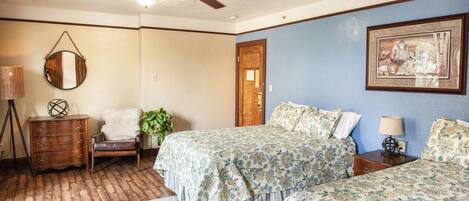 A bedroom with two beds, a ceiling fan, a wooden dresser, a chair, a lamp, and a framed picture on the wall.