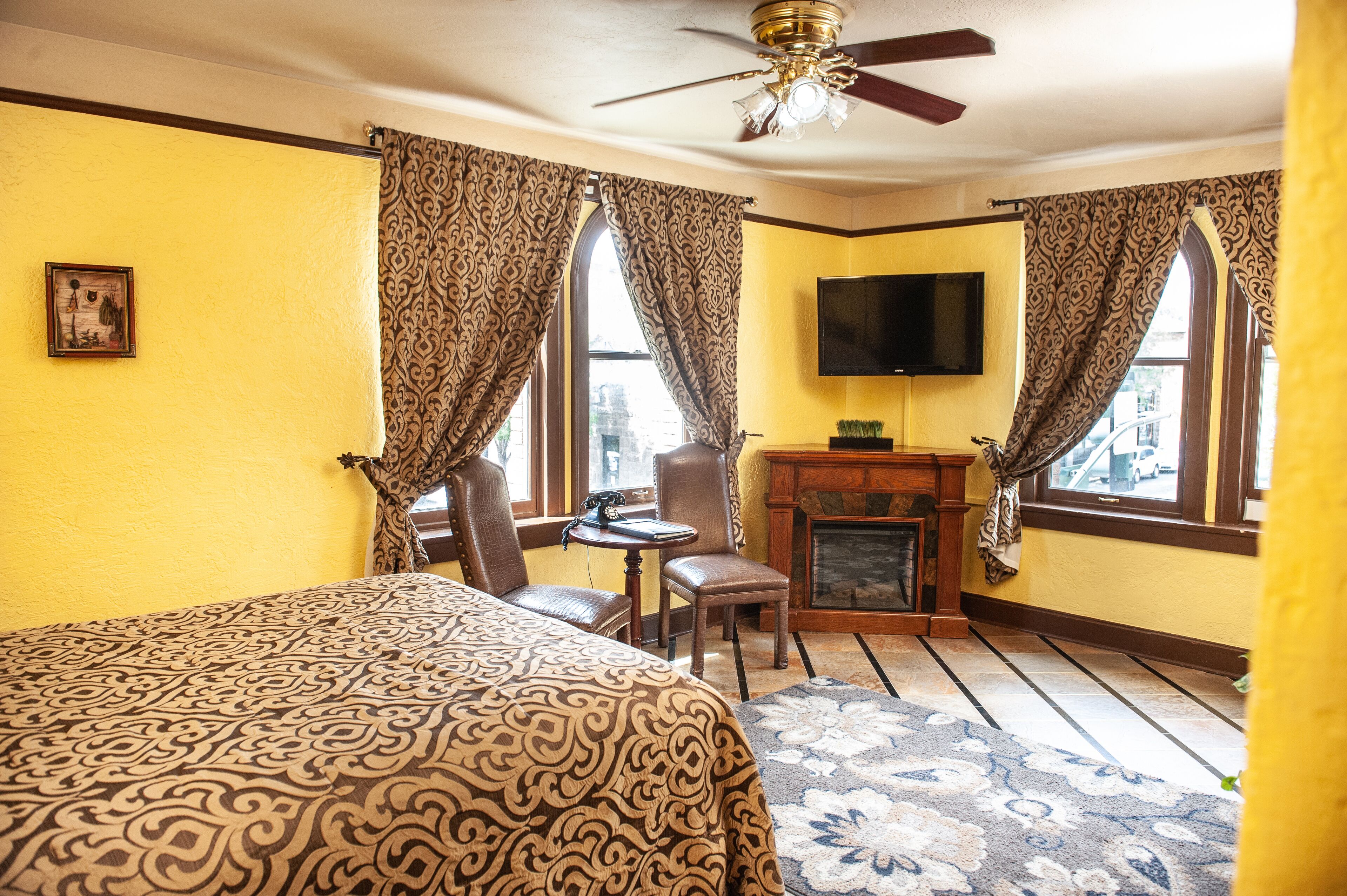 A hotel room with a bed, a desk with a chair, a fireplace, and a television mounted on the wall.