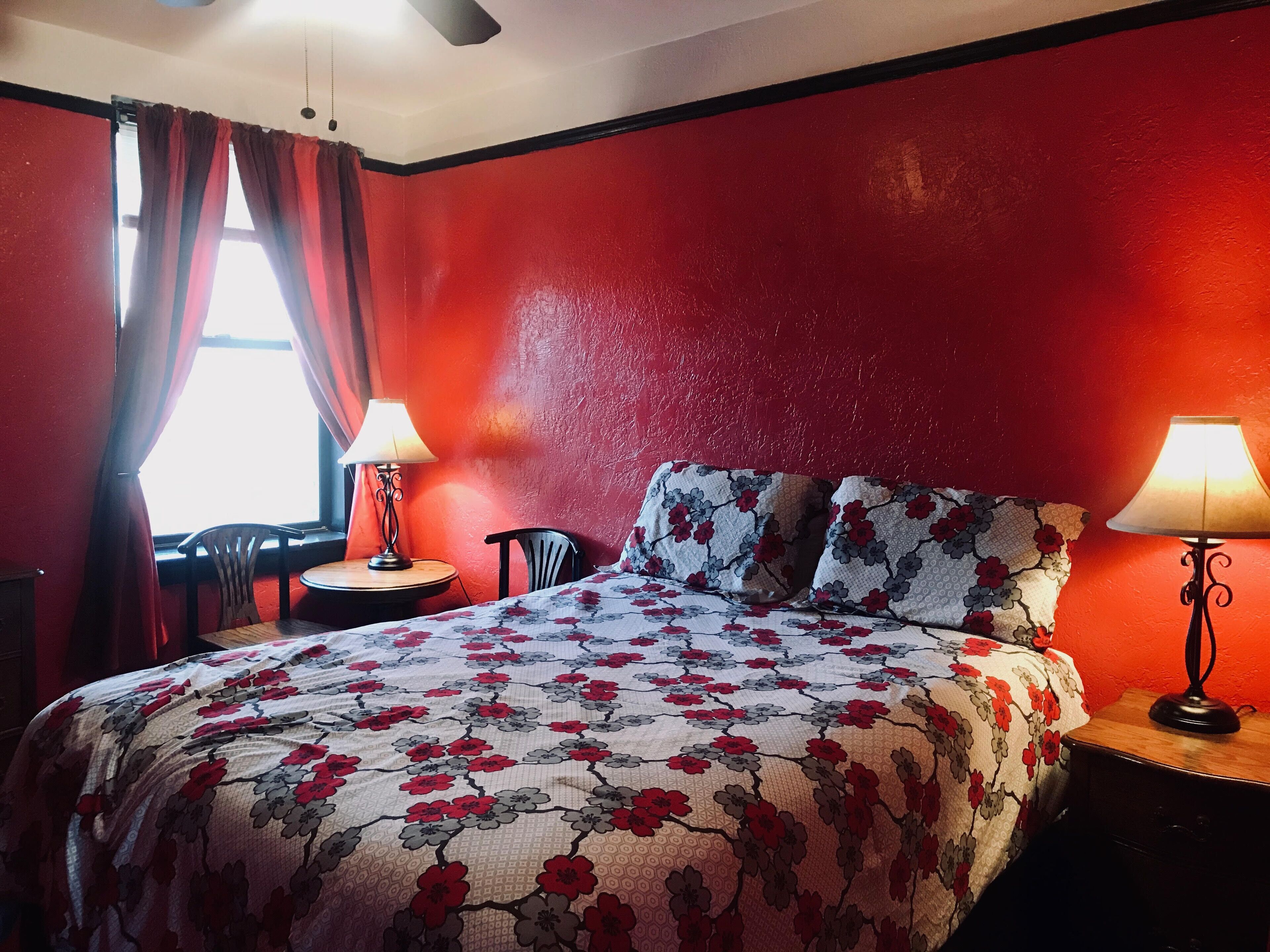 A room with a bed, two lamps, a chair, and a table.