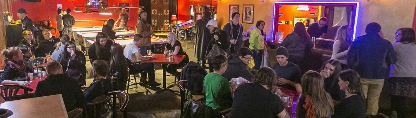 A crowded indoor dining area with tables and chairs, a bar area with stools, and a counter.