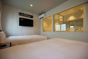 Une chambre d’hôtel avec deux lits, une télévision, un panneau indiquant la direction de l’hôtel, et une grande fenêtre donnant sur la salle de bain.