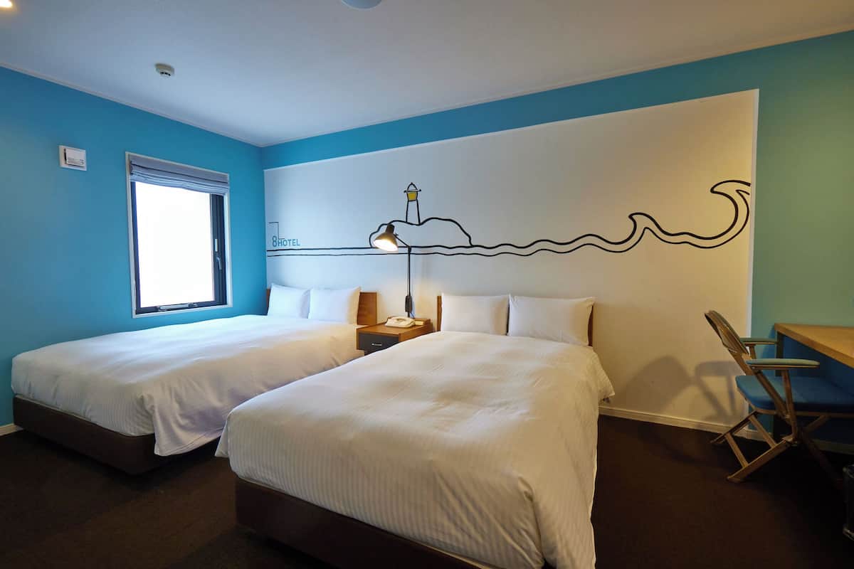 Una habitación de hotel con dos camas, un escritorio, una silla, un ventanal y un mural en la pared.