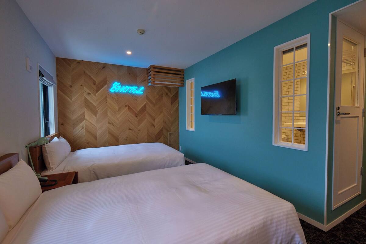 Habitación de hotel con dos camas, un televisor y un letrero de neón en la pared.