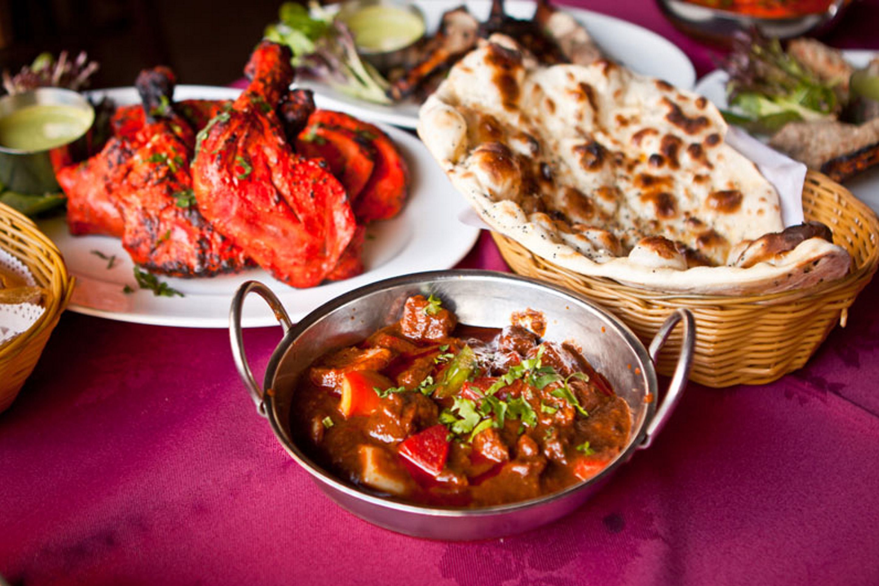 Una mesa con diversos platos, incluyendo pollo a la parrilla, pan naan y un tazón de guiso.