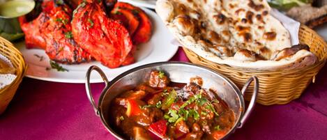 A table with various dishes including grilled chicken, naan bread, and a bowl of stew.