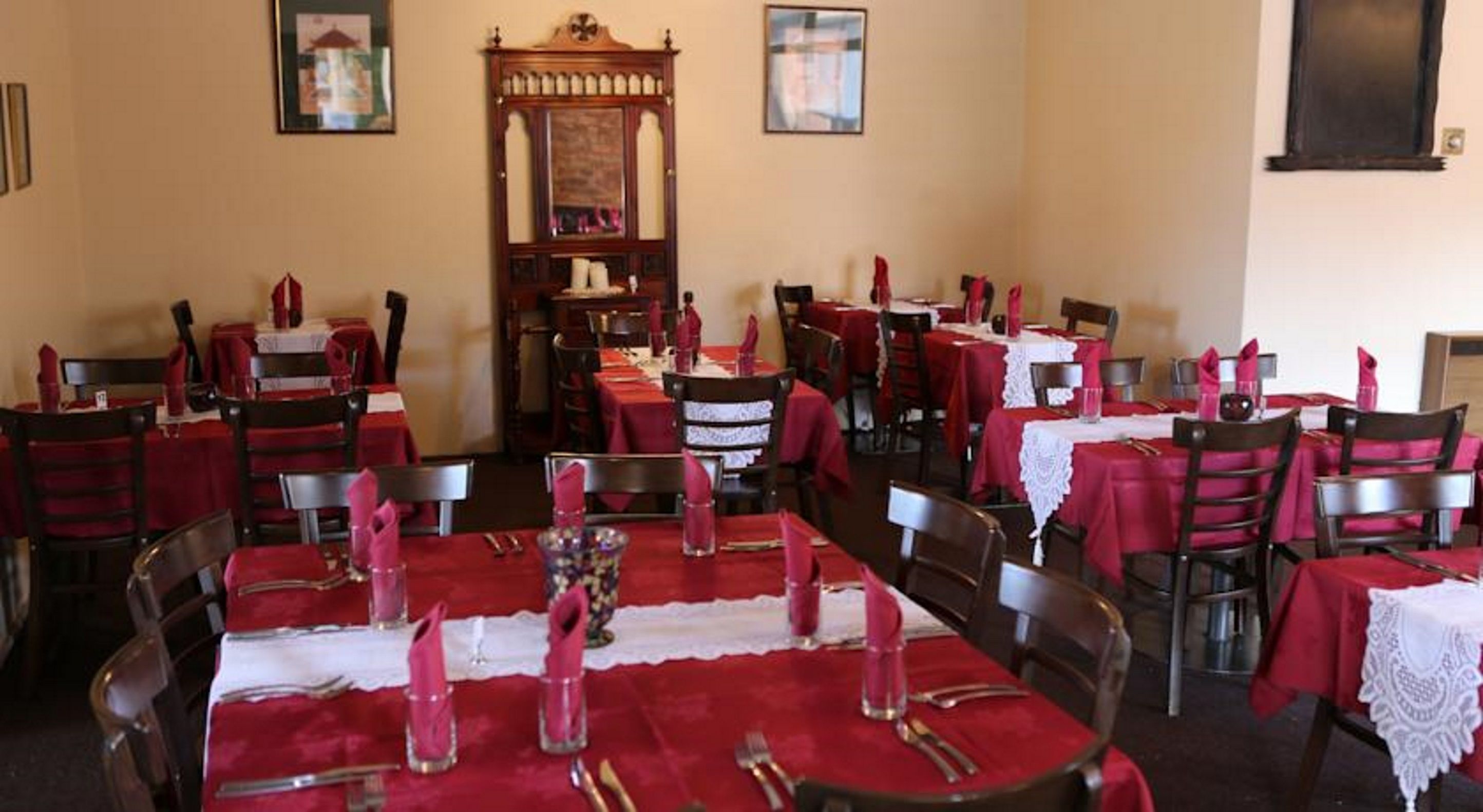 A dining area with tables set for multiple people, each with red tablecloths and white lace doilies.