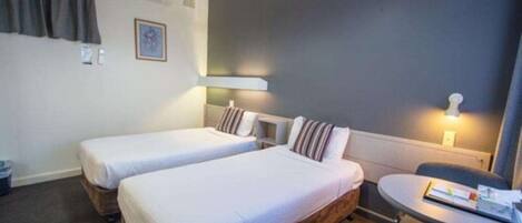 A hotel room with two single beds, a small table, and a chair.