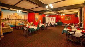 A restaurant with a mural of the Taj Mahal, red walls, and wooden beams. Tables are set with white tablecloths and red napkins.