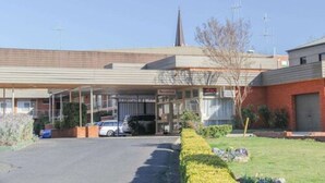 A motel with a covered parking area, a visible sign for 'Reception', and a church spire in the background.