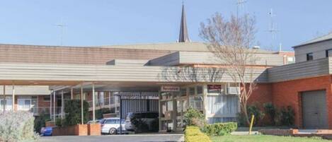 A motel with a covered parking area, a visible sign for 'Reception', and a church spire in the background.