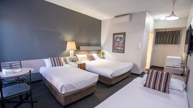 A hotel room with two single beds, a small table with a chair, a desk, and a TV.