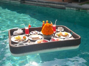 A floating breakfast tray with various food items and drinks by a pool.