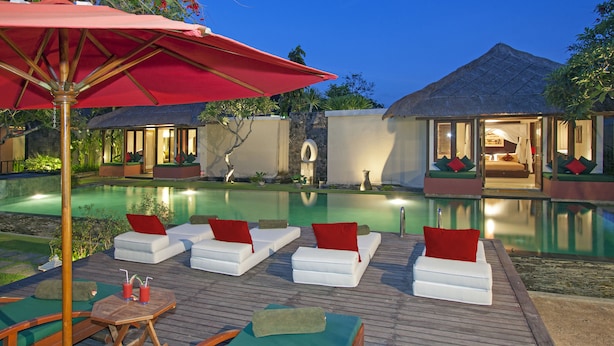 A poolside area with lounge chairs and a table, surrounded by a wooden deck and a red umbrella. - Imani Villas (Kerobokan)