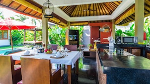 A restaurant with a tropical theme, featuring a thatched roof, wooden furniture, and a pool in the background. - Imani Villas (Kerobokan)
