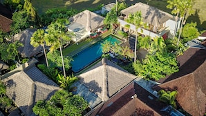 An aerial view of a residential area with a swimming pool surrounded by lush greenery and palm trees. - Imani Villas (Kerobokan)