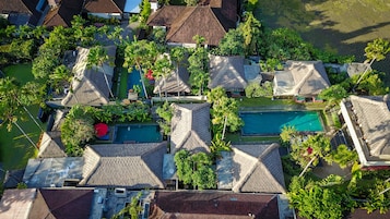 Vista aérea de um resort com vários edifícios no estilo de bangalôs, uma piscina central e vegetação exuberante.
