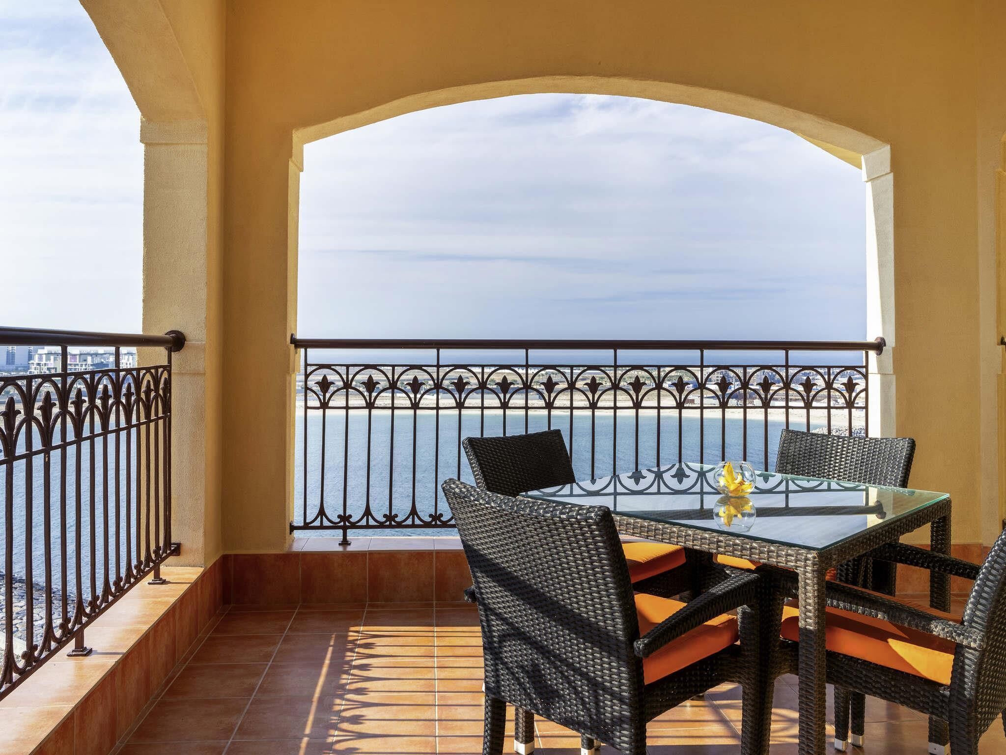 A balcony with a table and chairs, a railing, and a view of the sea.