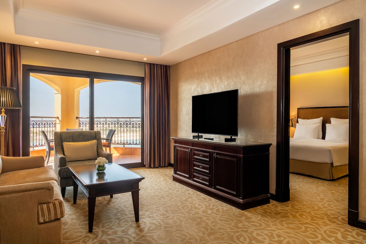 A hotel room with a large bed, a TV, a sofa, and a balcony with curtains.