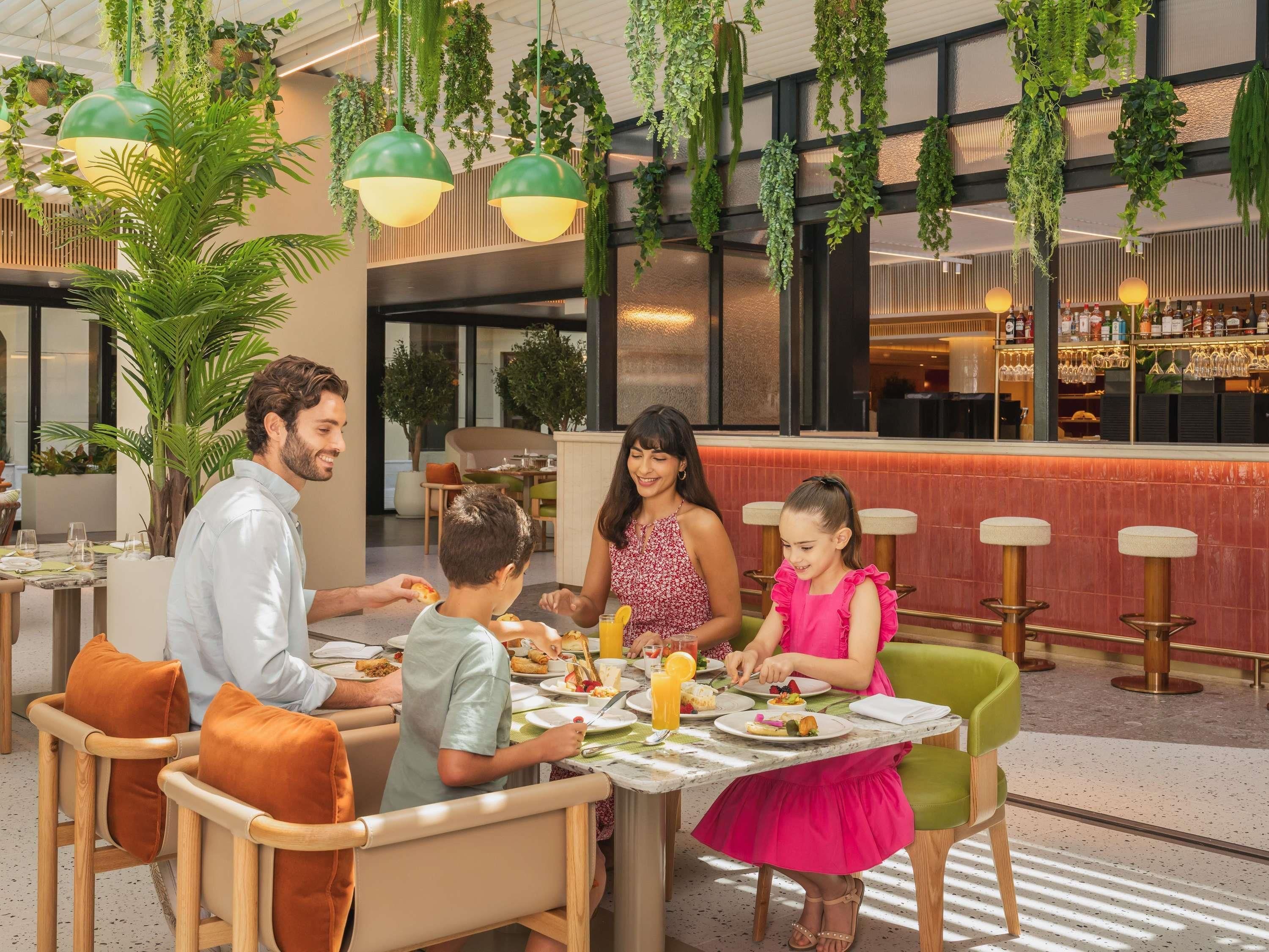 A family dining in a modern restaurant with hanging plants, a bar, and a casual seating area.