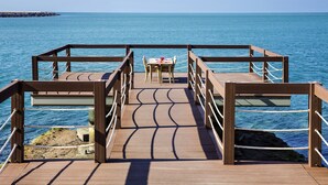 A wooden deck with a table and chairs facing the sea.