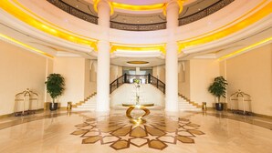 A grand, multi-level atrium with a central staircase, ornate railings, and a patterned floor.