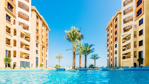 A swimming pool surrounded by palm trees and hotel buildings with balconies.