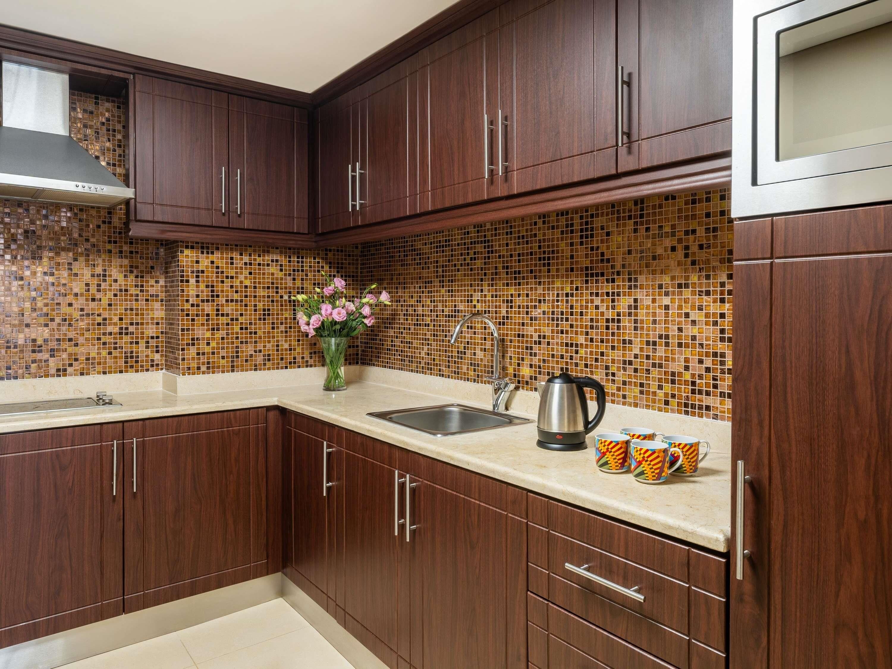 A kitchen with dark wood cabinets, a tiled backsplash, a stainless steel sink, and a kettle on the counter.